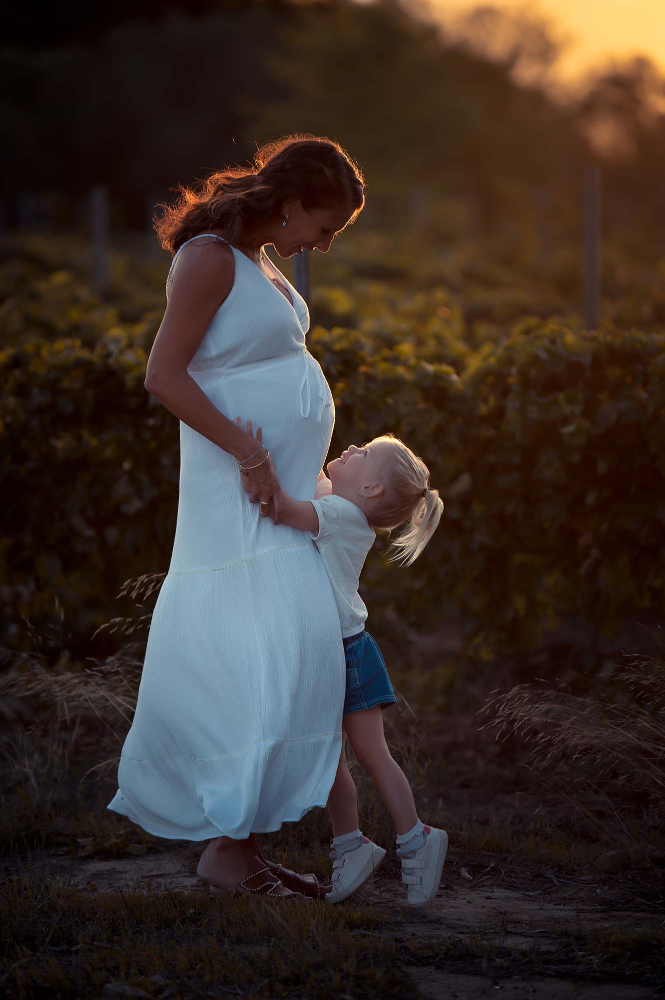 photos d'une femme enceinte accompagnée et de sa fille devant des vignes au coucher de soleil