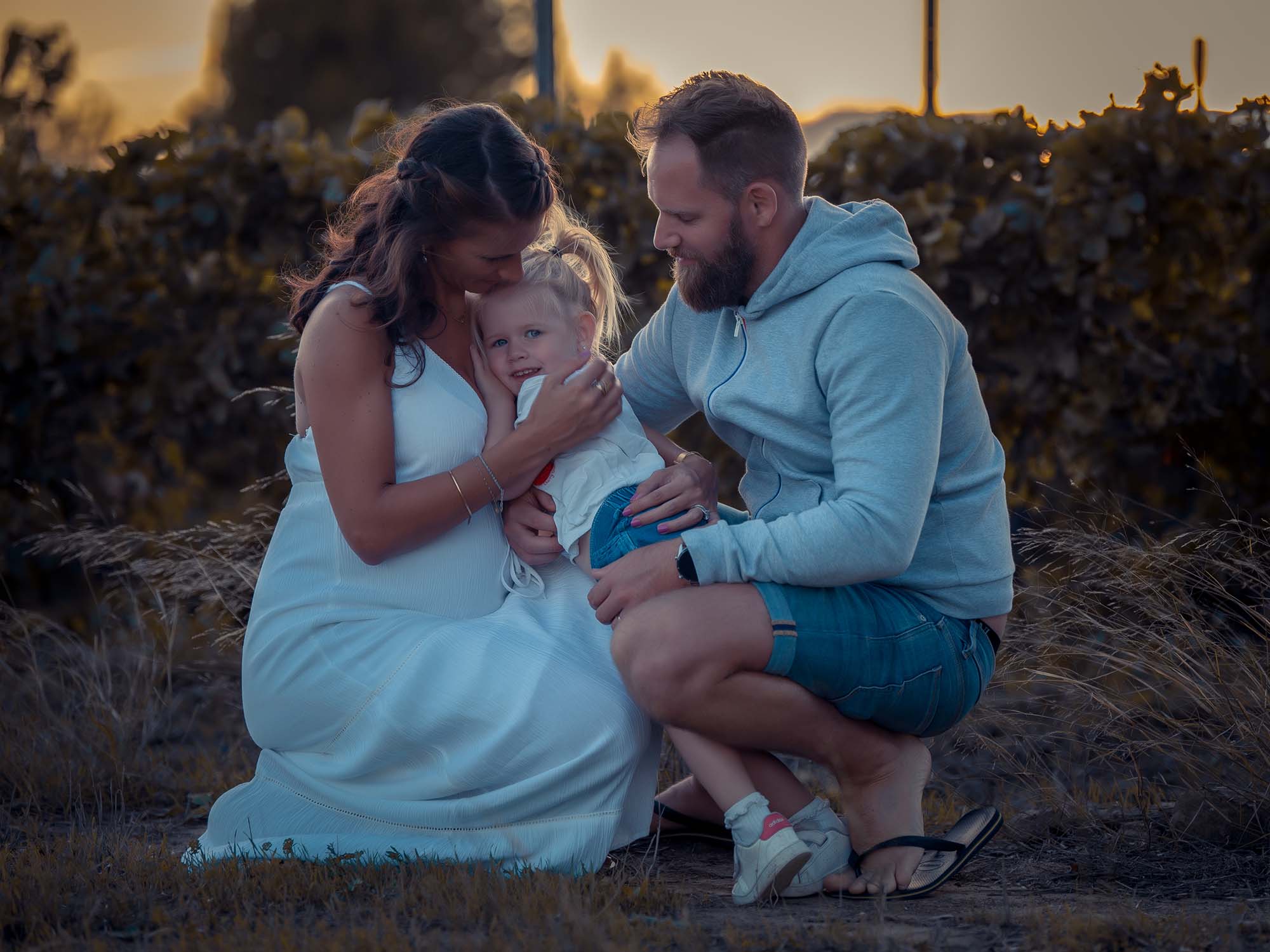 photos d'une femme enceinte accompagnée de son mari et de sa fille devant des vignes au coucher de soleil