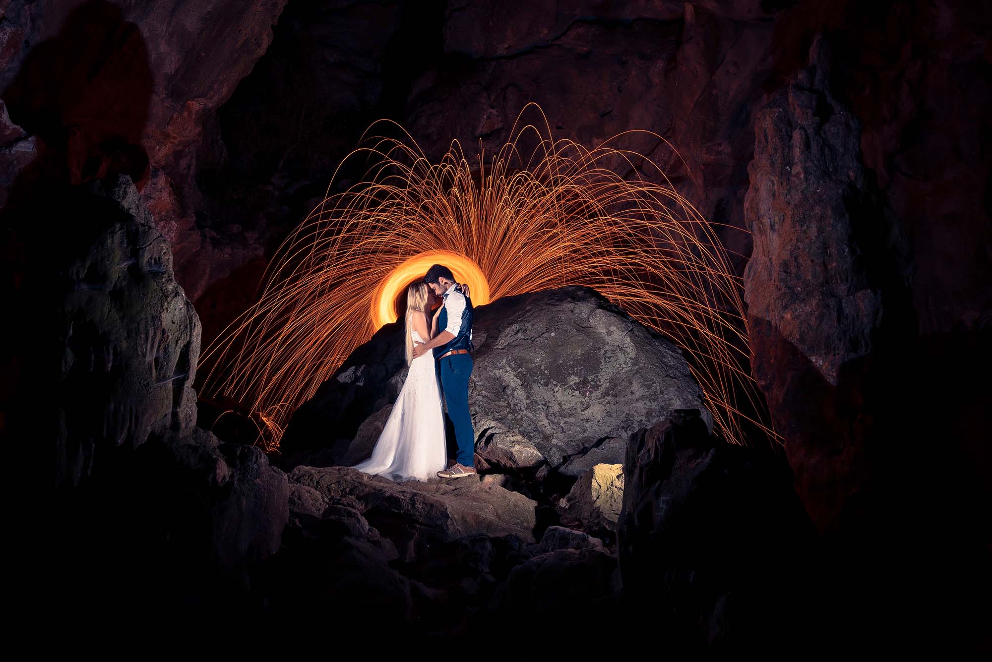 Photo d'un couple de jeunes mariés prises dans une grotte dans le noir avec des étincelles derrière