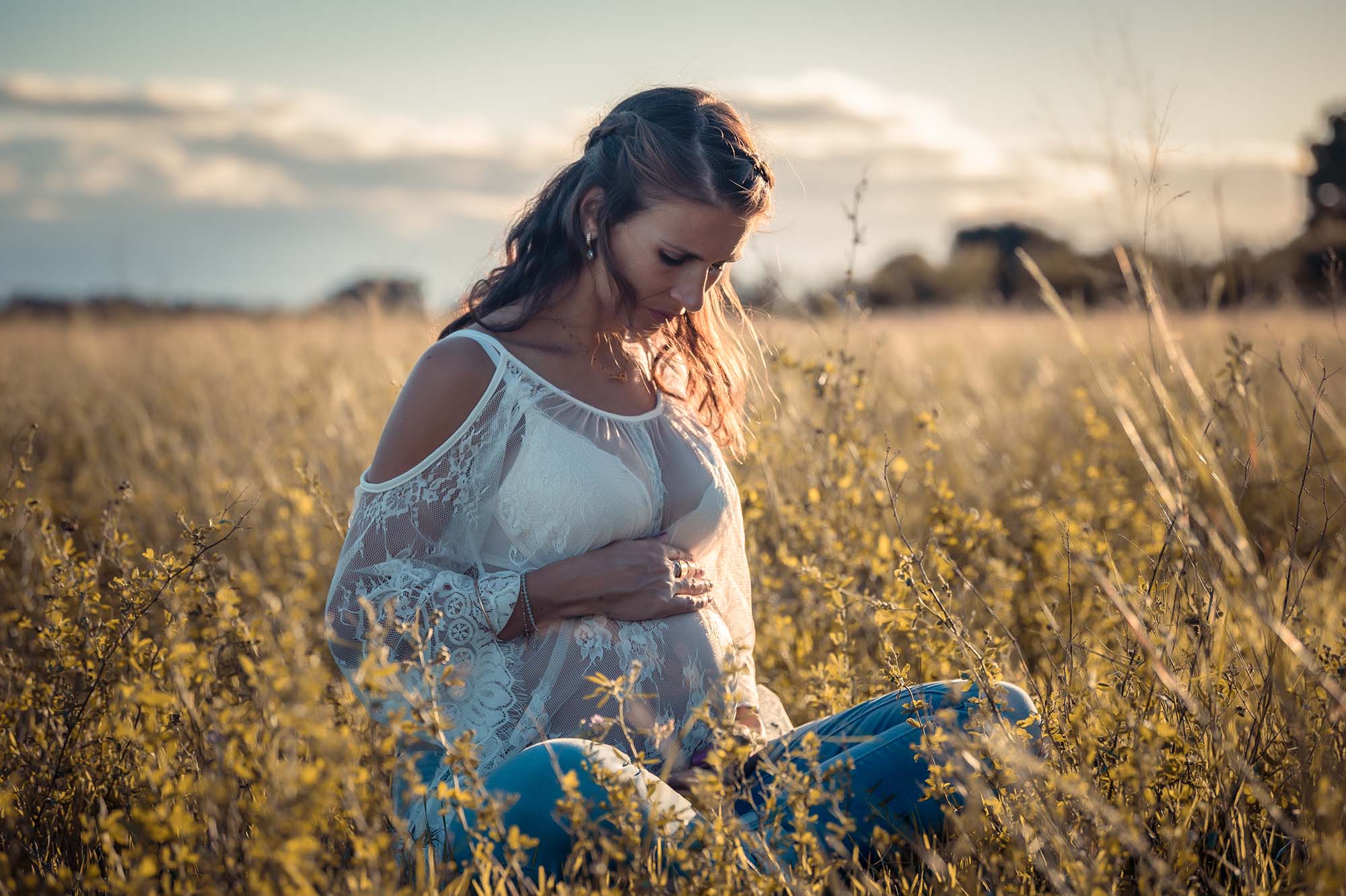 photo d'une femme enceinte assise dans un champ au coucher de soleil
