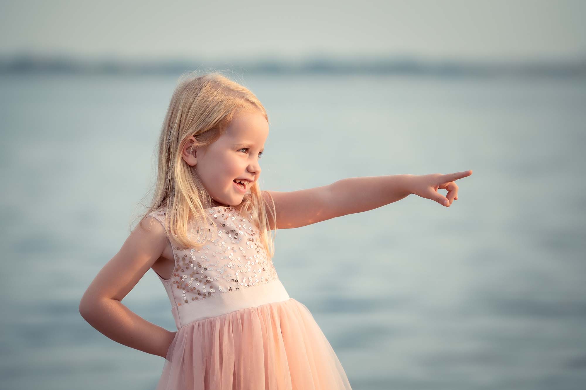 photo d'une petite fille habillée en robe rose qui montre quelque chose avec son doigts
