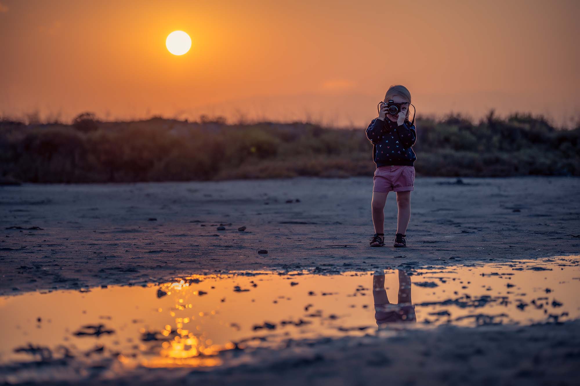 photo d'une petite fille au coucher de soleil tenant un appareil photo dans ses mains