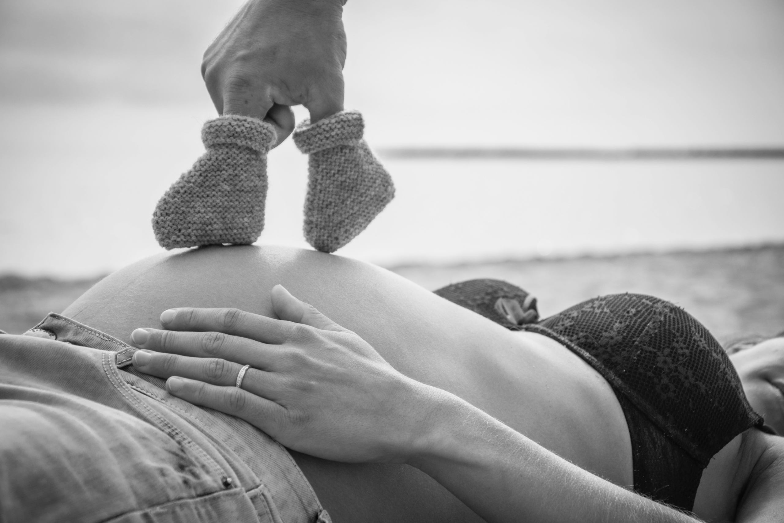 gros plan noir et blanc d'un ventre de femme enceinte où l'on voit des chaussons de bébé en laine