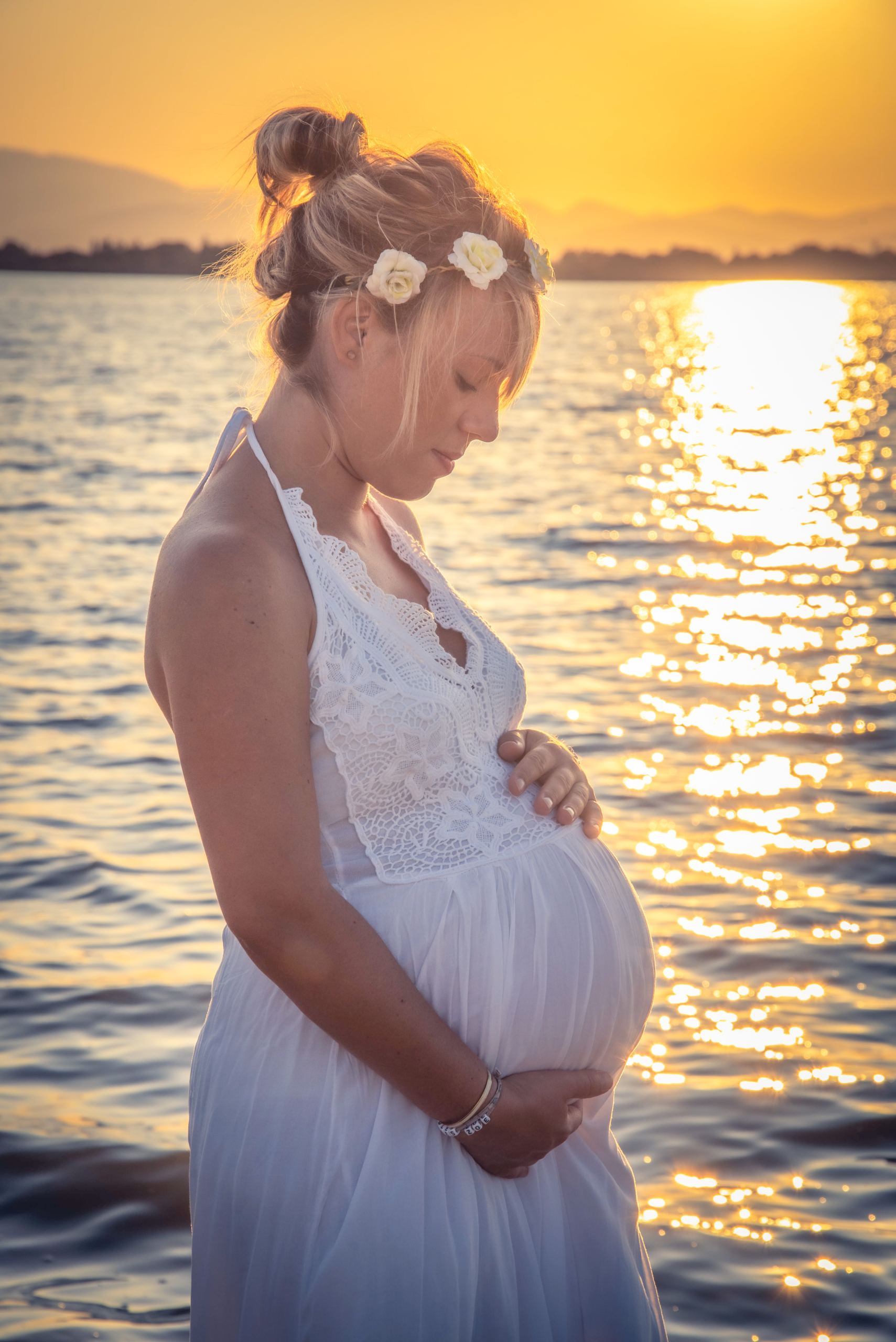 photo d'une femme enceinte prise de profil vêtue d'une robe blanche au coucher de soleil