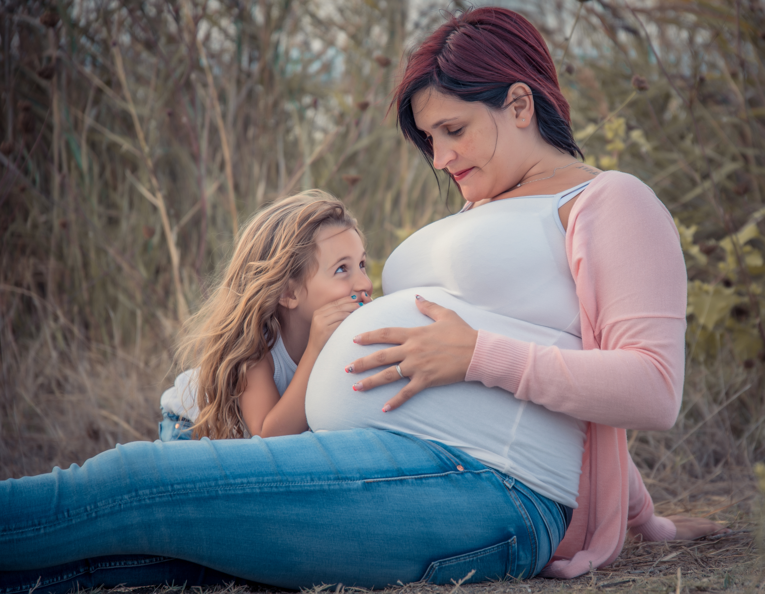 photo d'une femme enceinte sur laquelle on voit une petite fille chuchoter un mot au ventre de sa maman