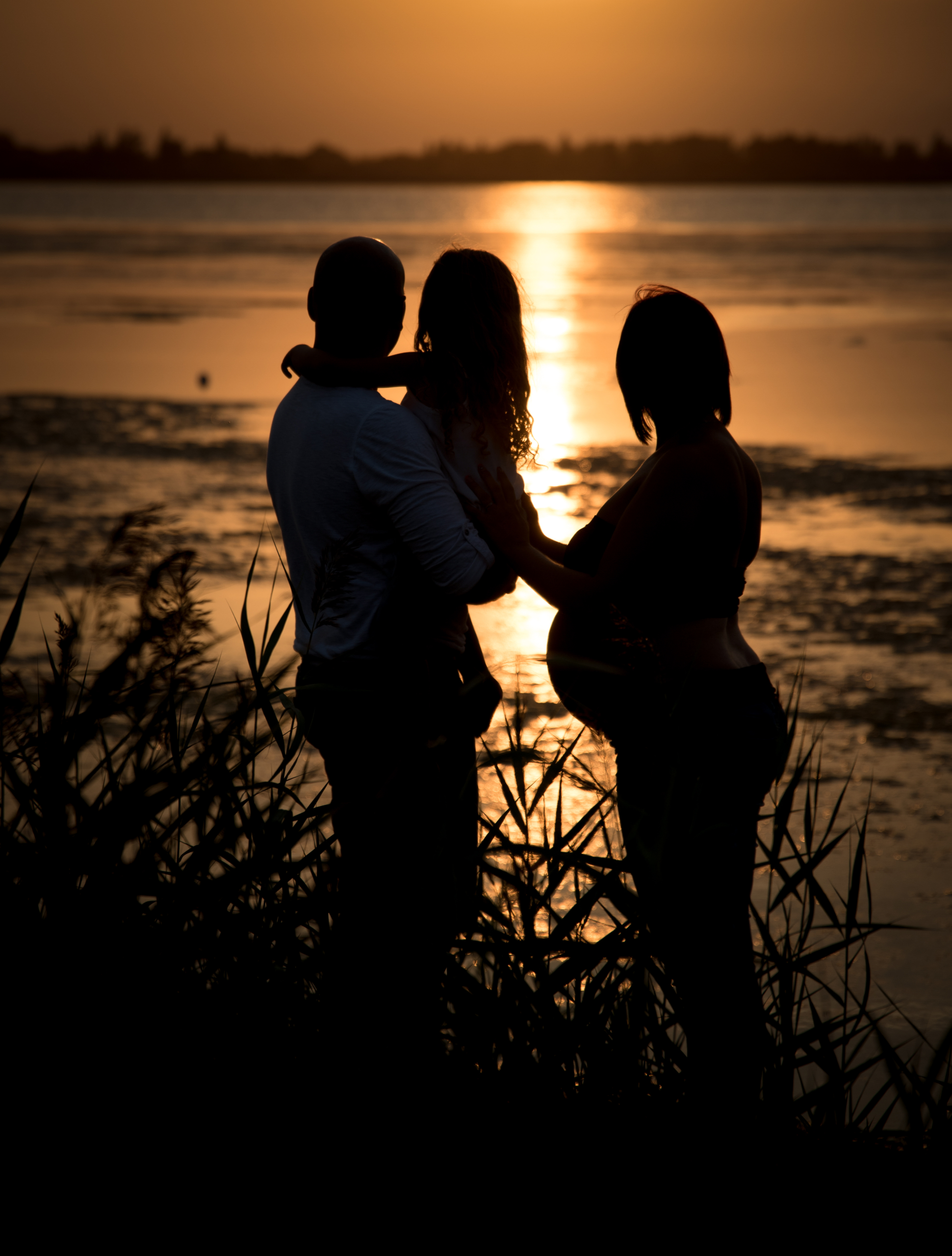 photo en contre jour d'une famille avec une femme enceinte en bord d'étang