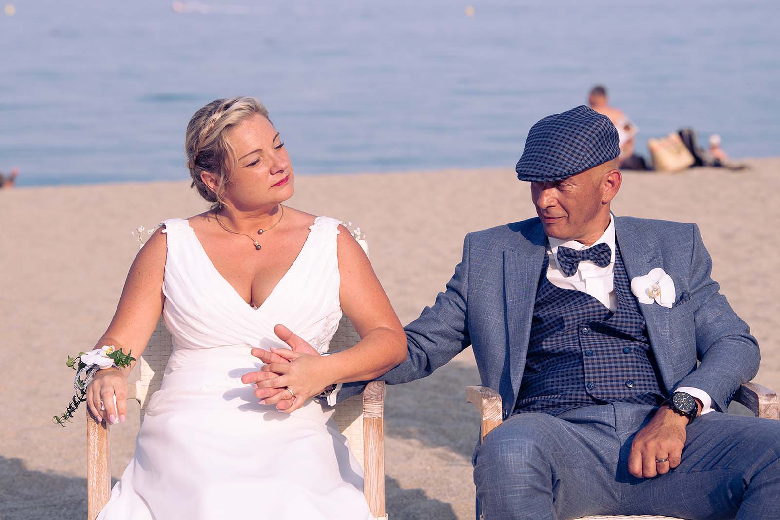deux mariés assis se tenant la main à la plage