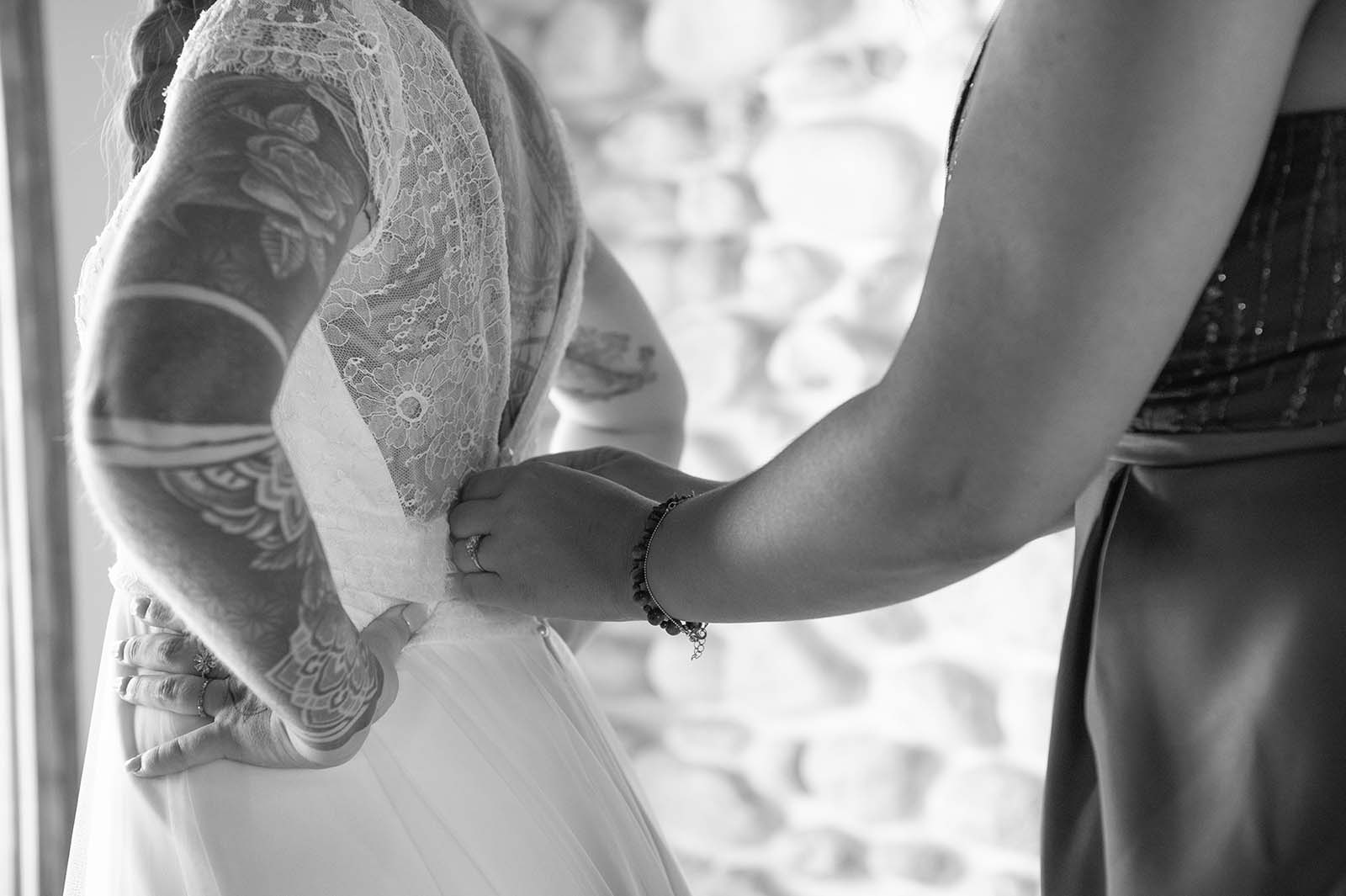 photo noir et blanc d'un gros plan sur une main en train de boutonner la robe d'une mariée