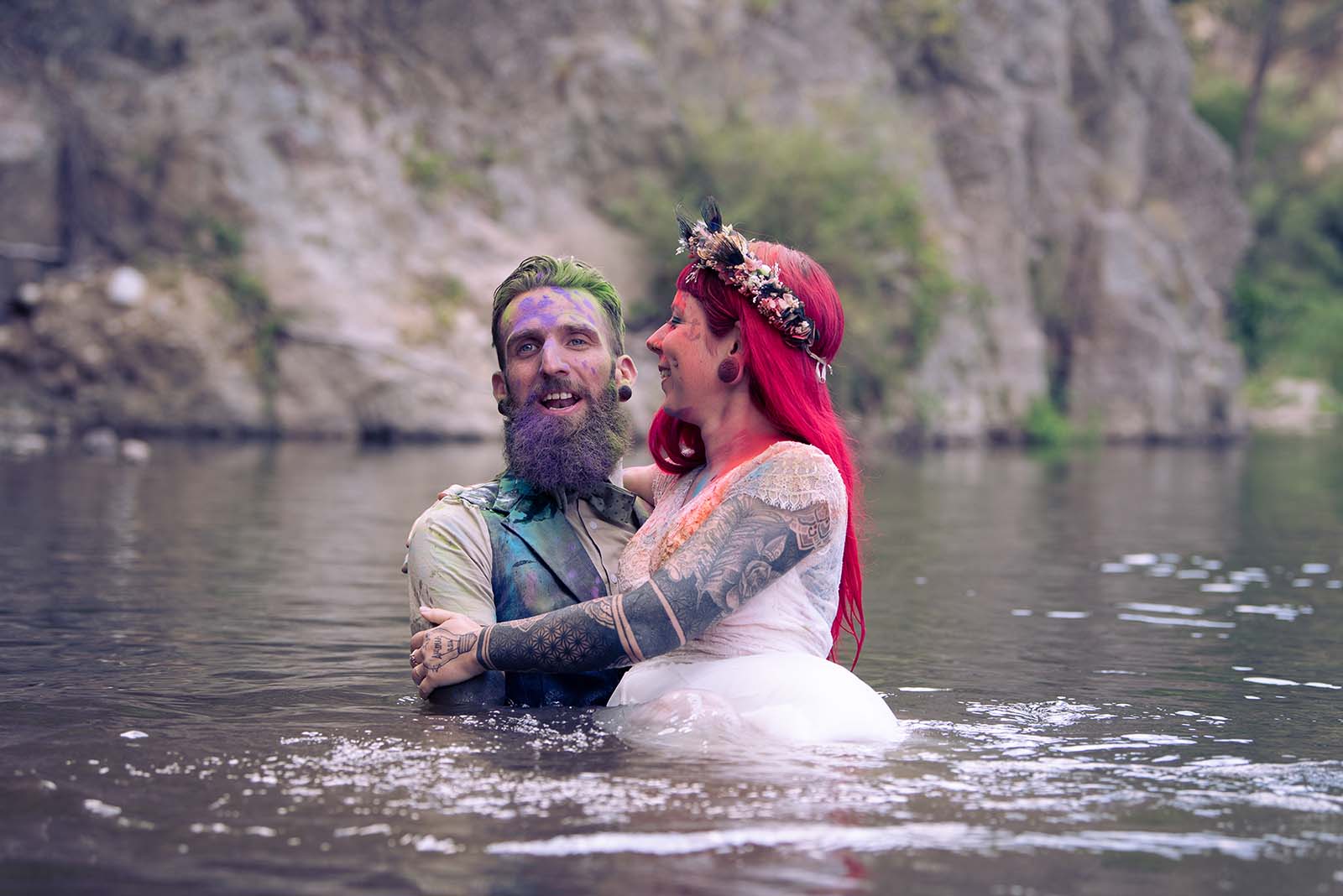 couple de mariés lors de la séance trash the dress, ils sont dans l'eau ils sont couverts de poudre colorée