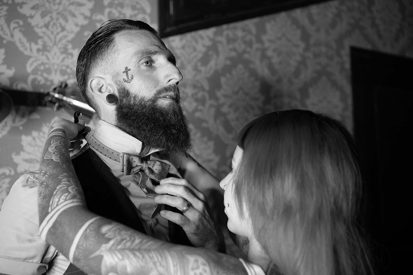 photo noir et blanc d'une femme accrochant le nœud papillon d'un homme barbu