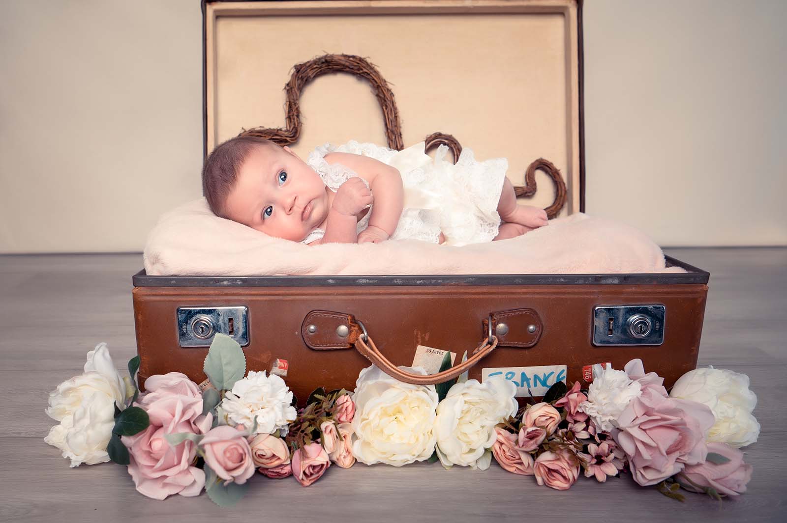 photo d'un bébé positionné sur le coté dans une vieille valise avec des fleurs sur le devant