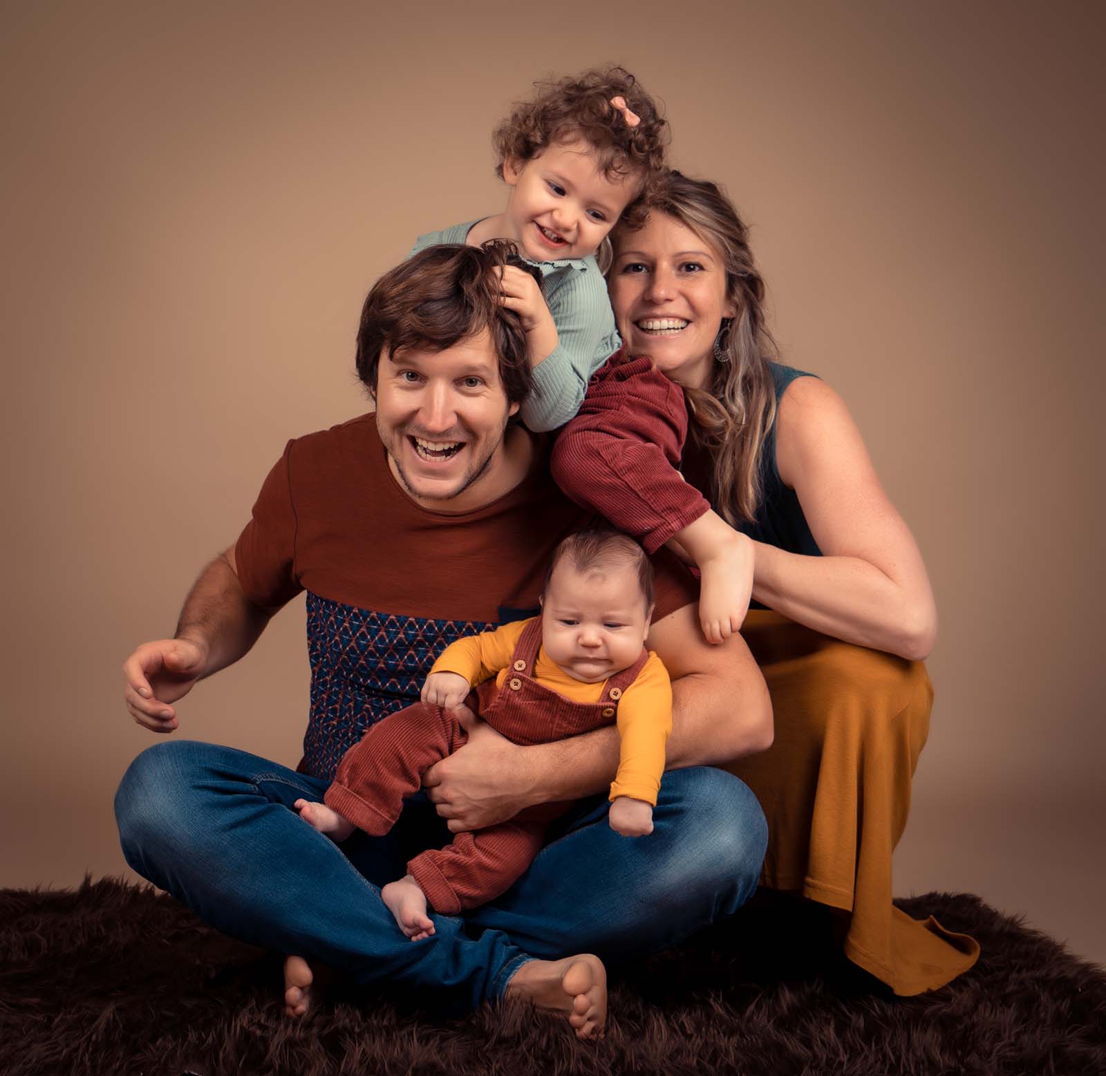 photo studio d'une famille assise au sol avec une petite fille et un bébé dans les bras de son papa