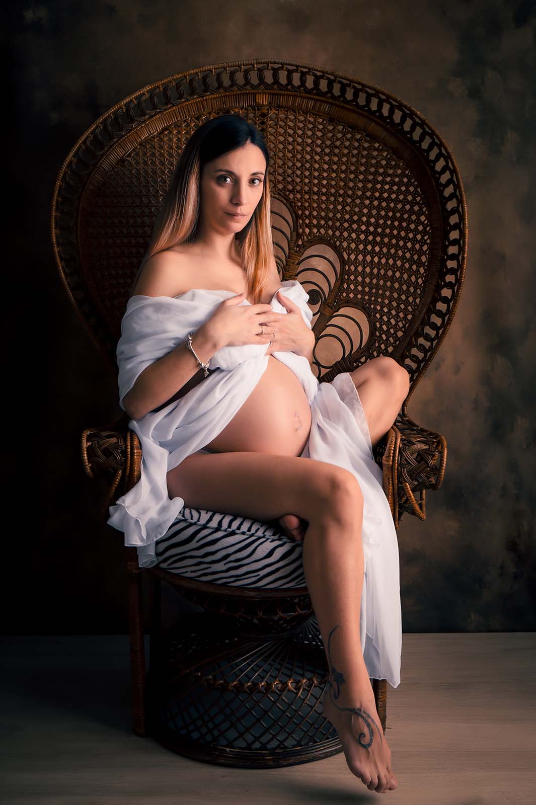 femme enceinte blonde aux cheveux longs vêtue d'un voile blanc et assise dans un fauteuil Emmanuelle