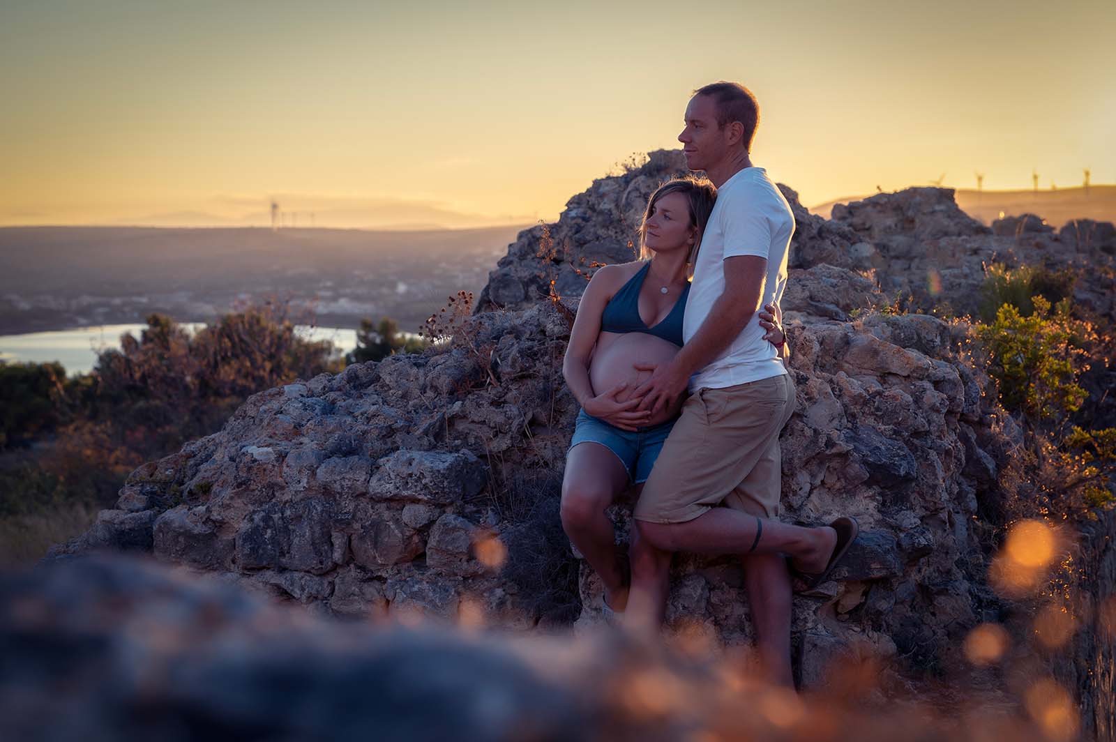 photo d'un couple au coucher de soleil, la femme est enceinte et ils sont appuyés sur des pierres
