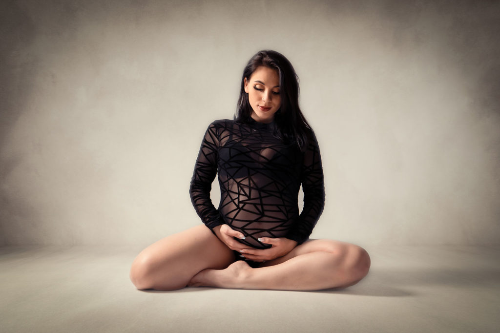 femme enceinte brune en body noir assise au sol .elle a le regard vers son ventre