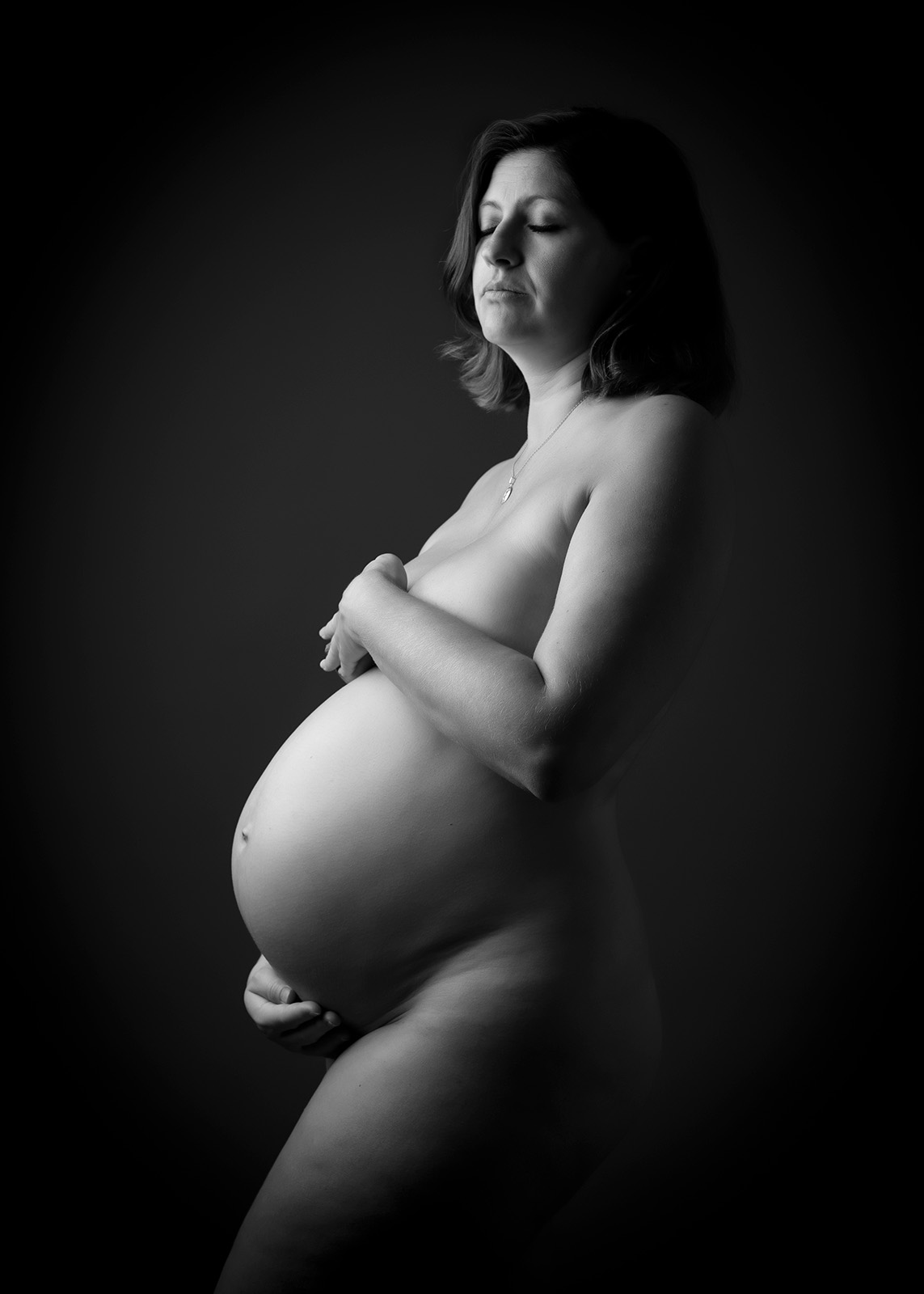 photo noir et blanc d'une femme enceinte nue cachant sa poitrine avec les mains