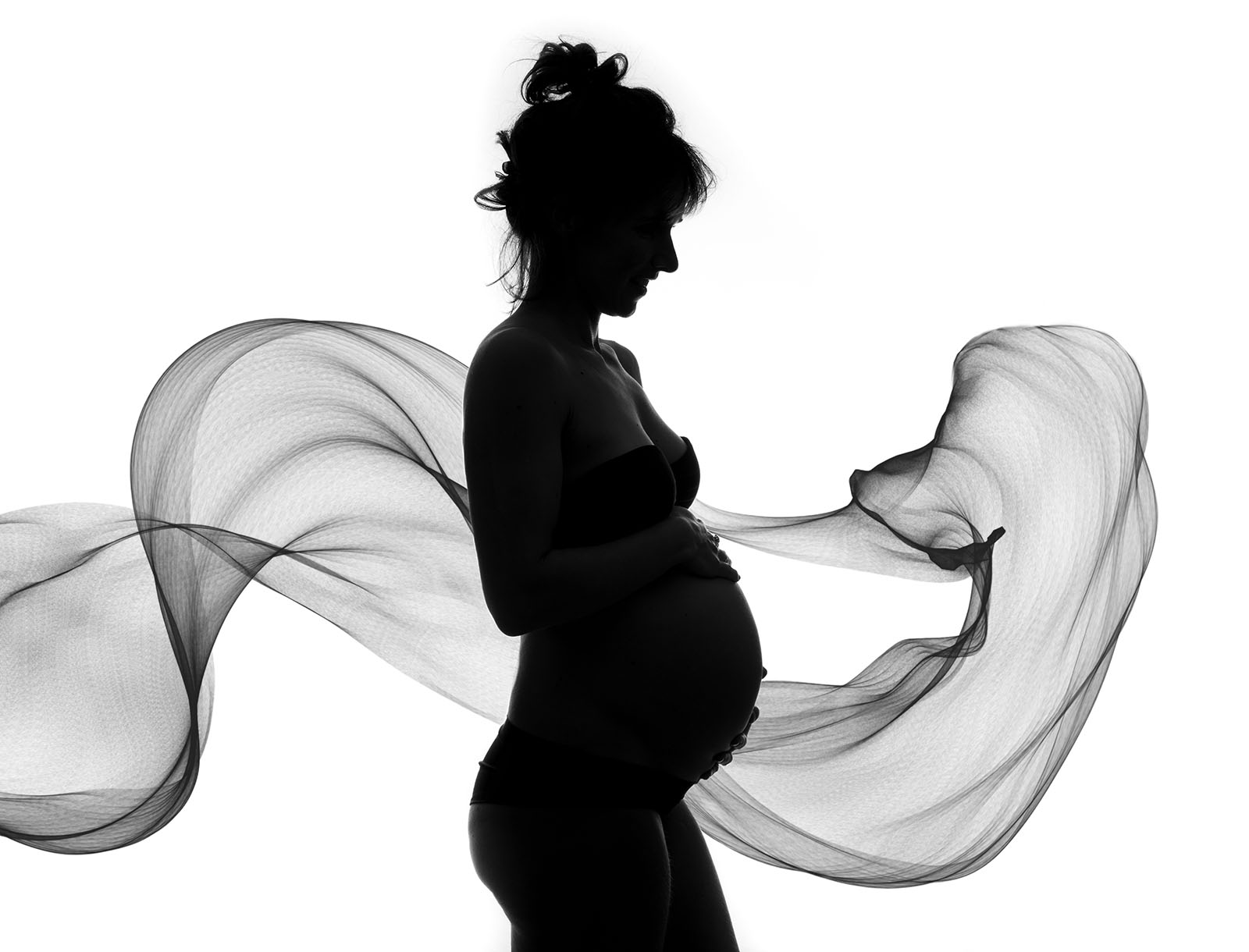 silhouette d'une femme enceinte à contre jour avec un voile qui vole derrière elle