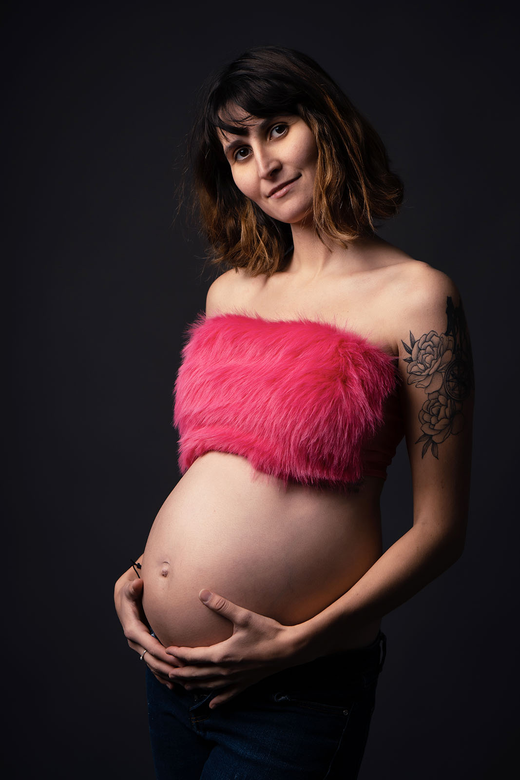 femme enceinte aux cheveux cours habillée avec un crop top rose à poils et un jean