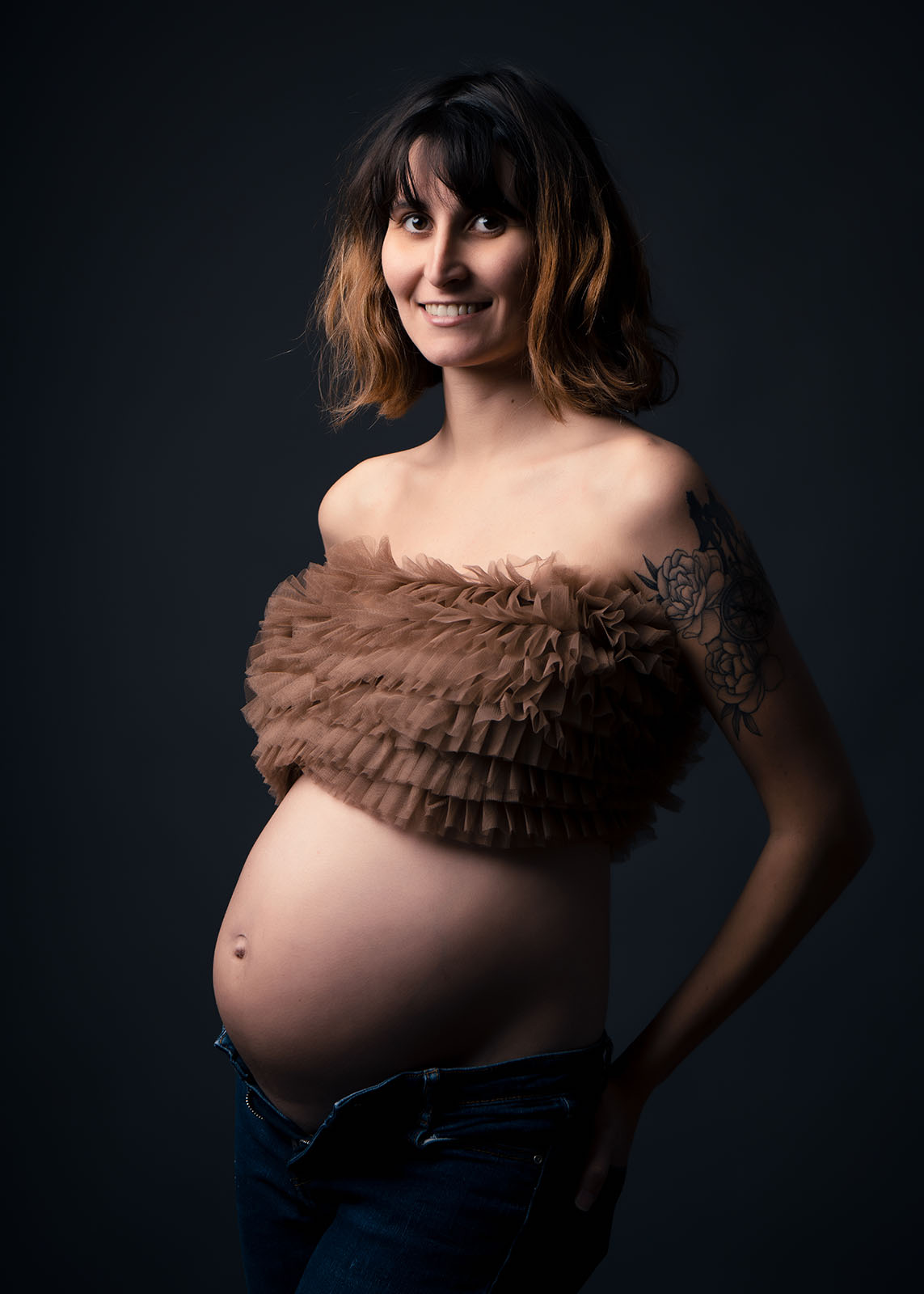femme enceinte aux cheveux cours habillée avec un crop top marron à froufrou et un jean