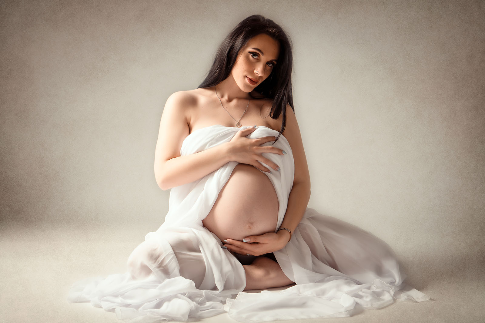 femme enceinte brune assise au sol et vêtue d'un voile blanc
