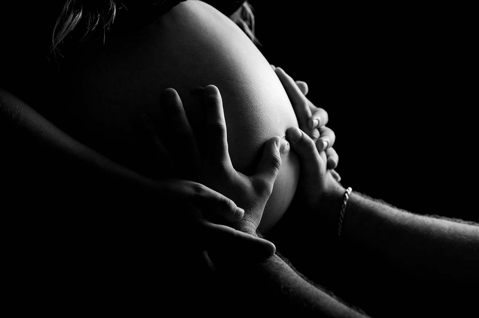 clair obscur d'un ventre de femme enceinte avec les mains d'un homme dessus