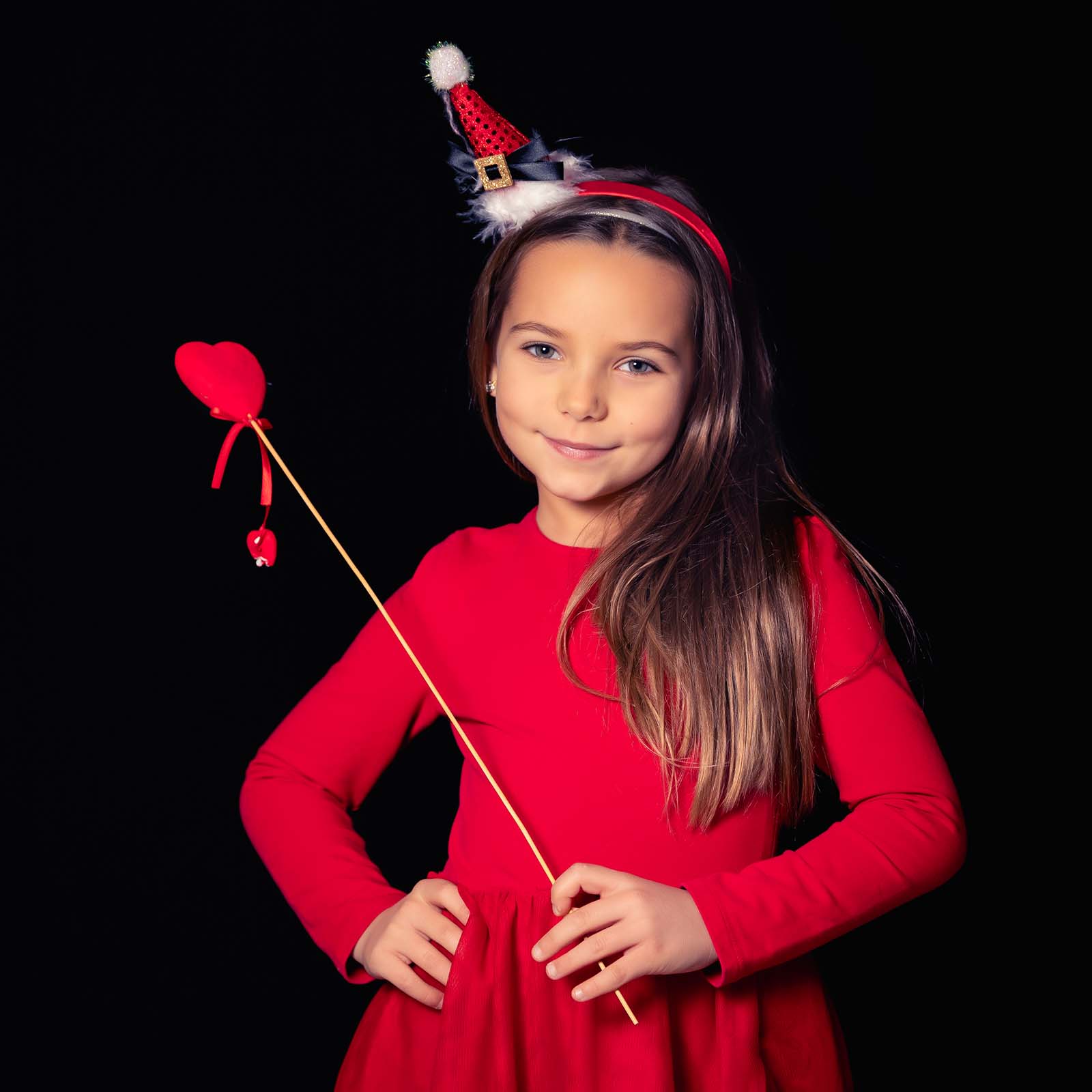 portrait d'une petite fille habillée en rouge avec un petit chapeau de noël et une baguette avec un cœur au bout