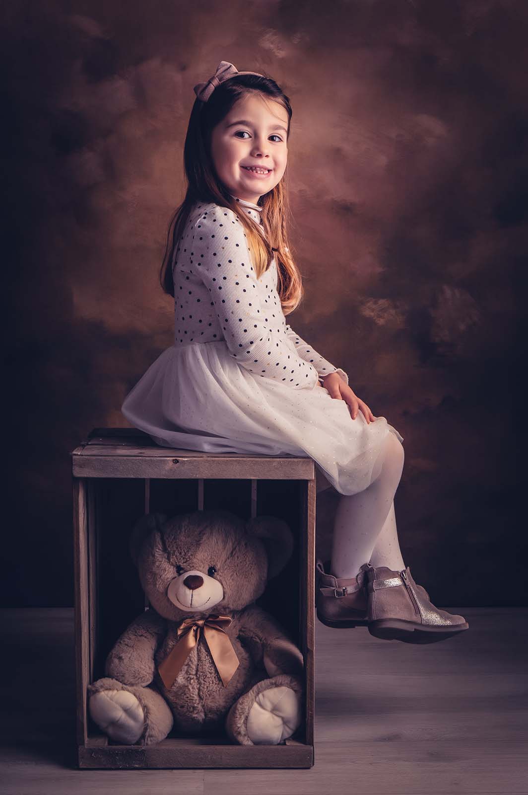 petite fille assise sur une caisse en bois avec un nounours dedans