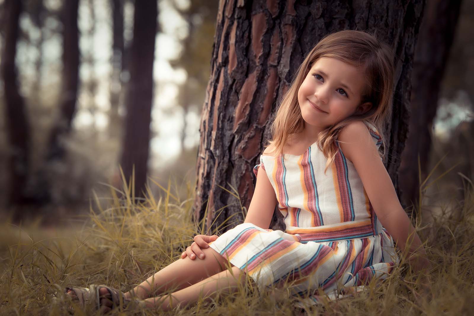 portrait d'une jeune fille assise dans l'herbe et appuyée contre un arbre