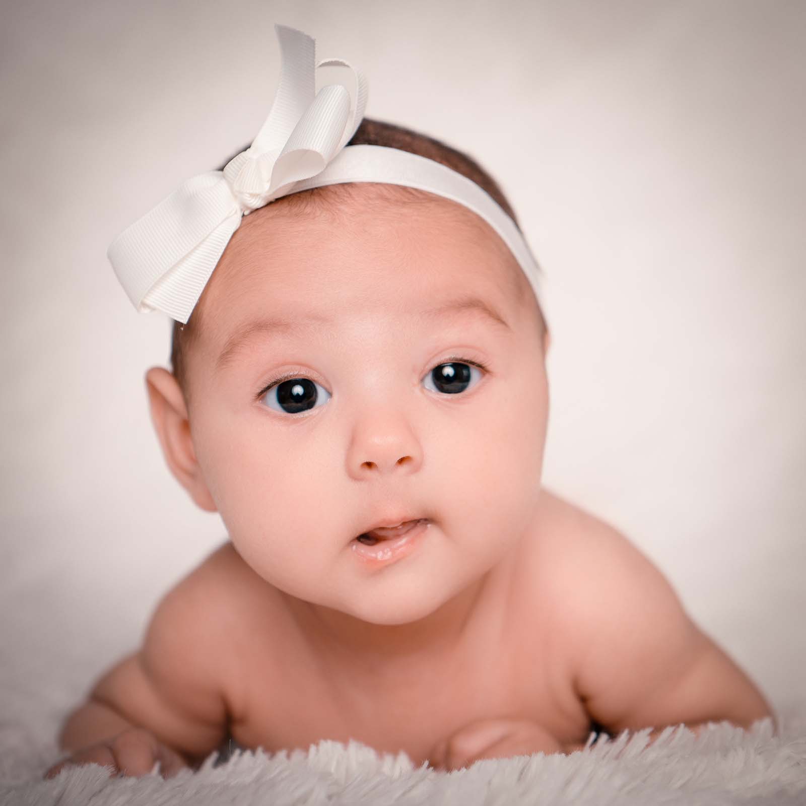 portrait de bébé se tenant allongé la tête relevée avec un petit nœud blanc dans les cheveux