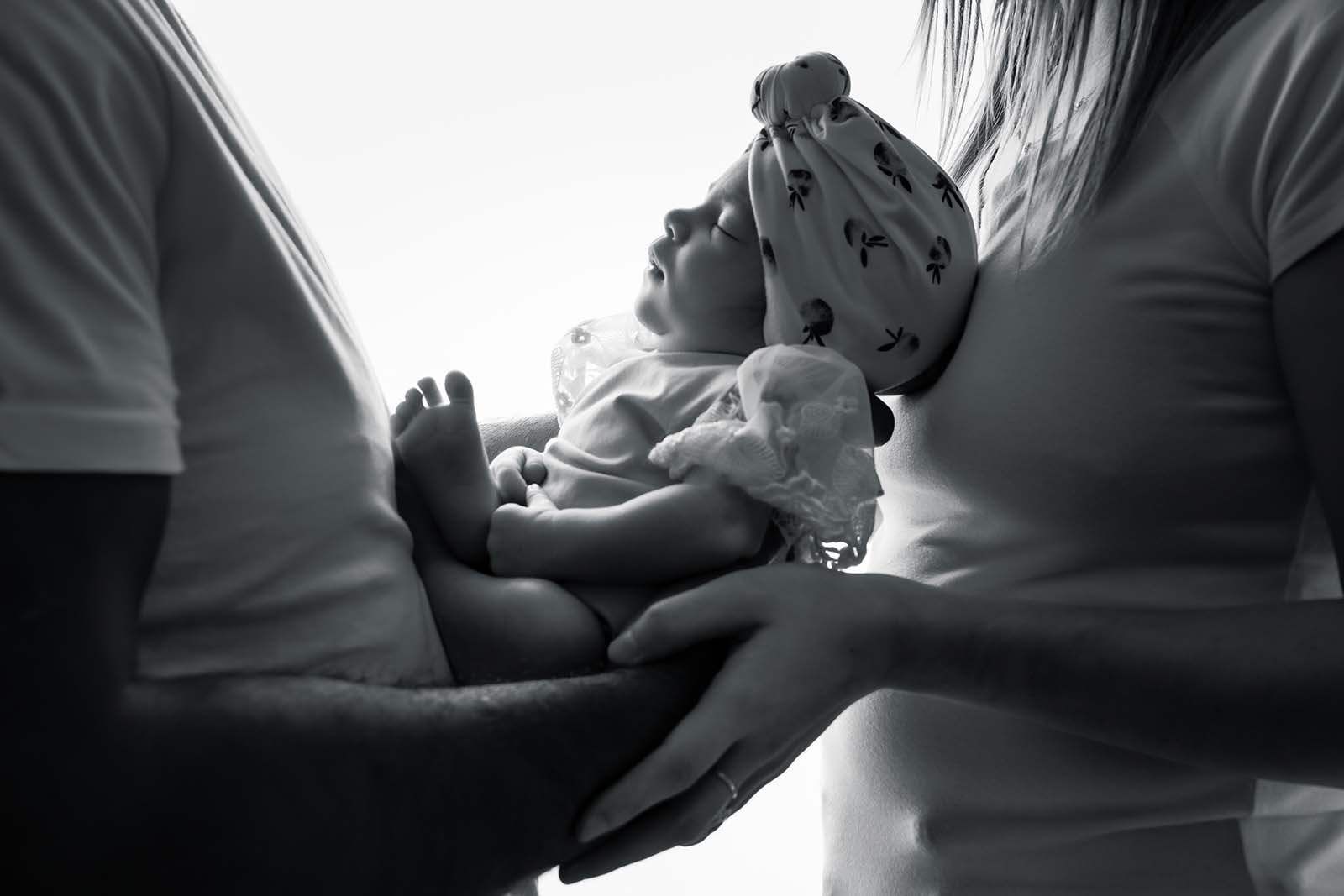 photo noir et blanc d'un bébé prise en contre jour dans les mains de ses parents
