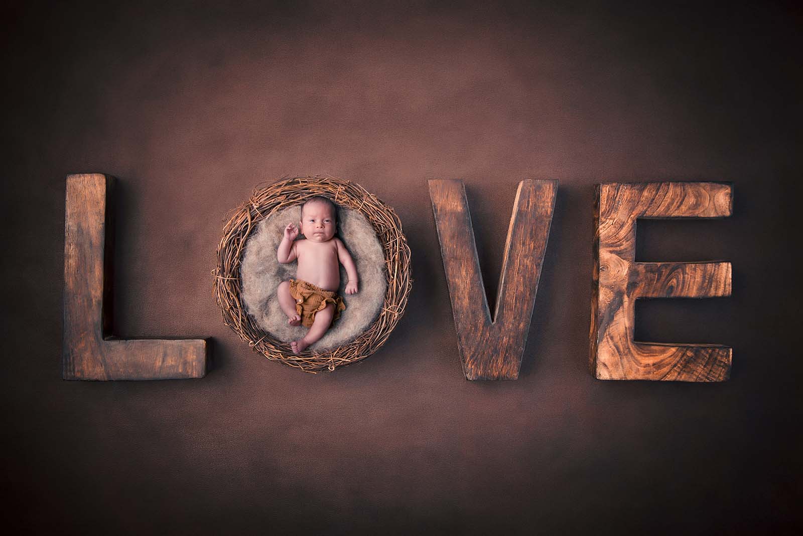 bébé dans un panier en osier avec des lettres en bois où il est écrit le mot love