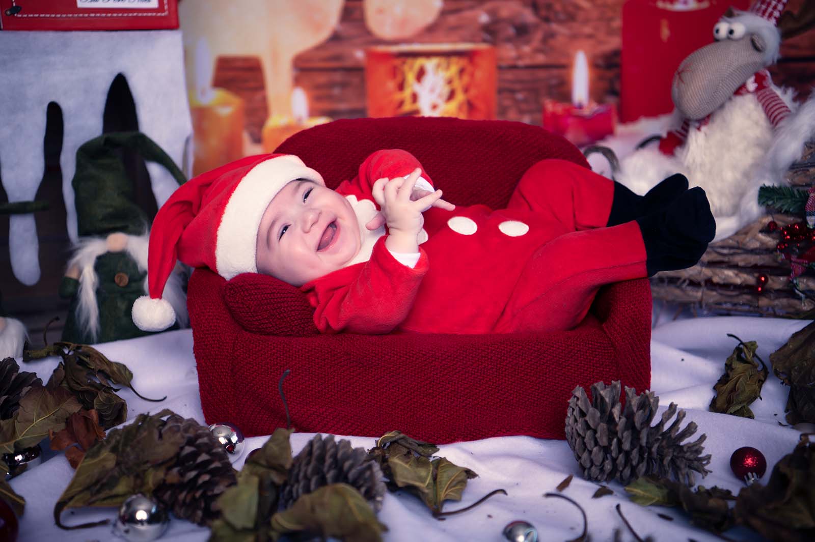 photo d'un bébé habillé en costume de père noël allongé dans un petit canapé