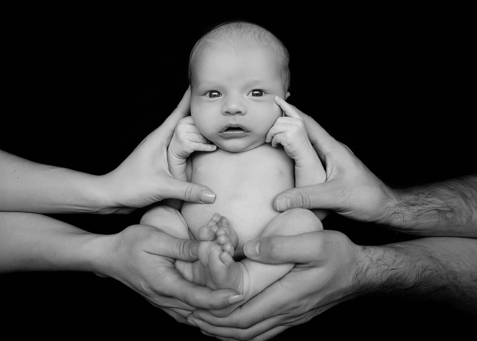 portrait de bébé noir et blanc entouré des mains de ses parents