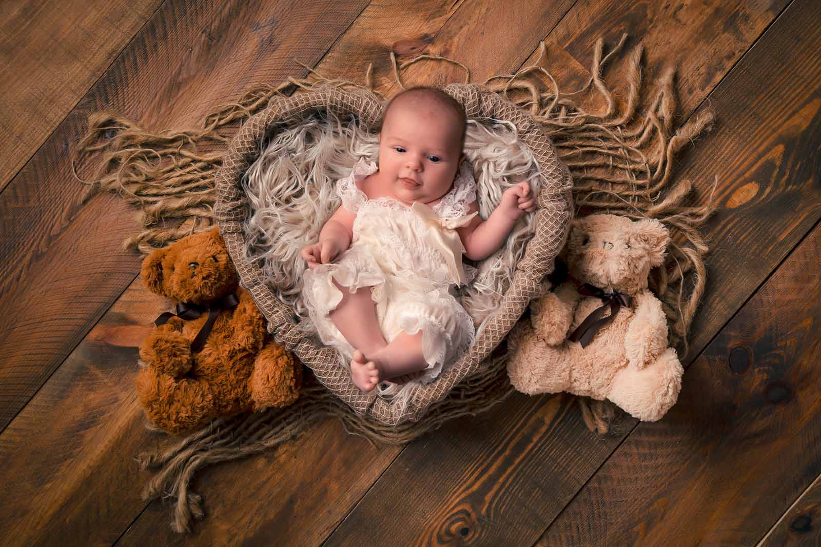 photo d'un bébé dans un contenant en forme de cœur entouré de deux ours en peluche