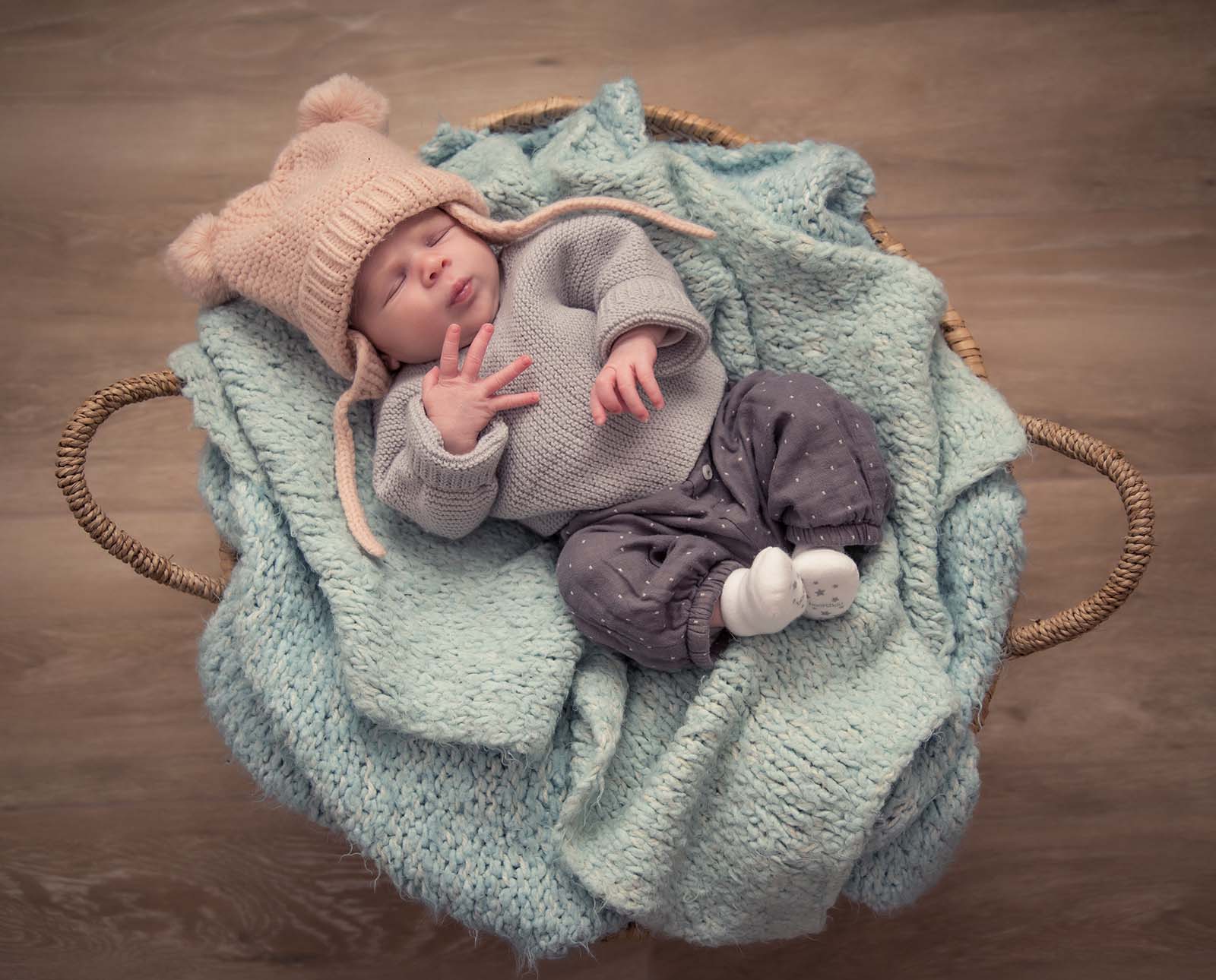 portrait d'un bébé dans un gros panier avec un bonnet sur la tête