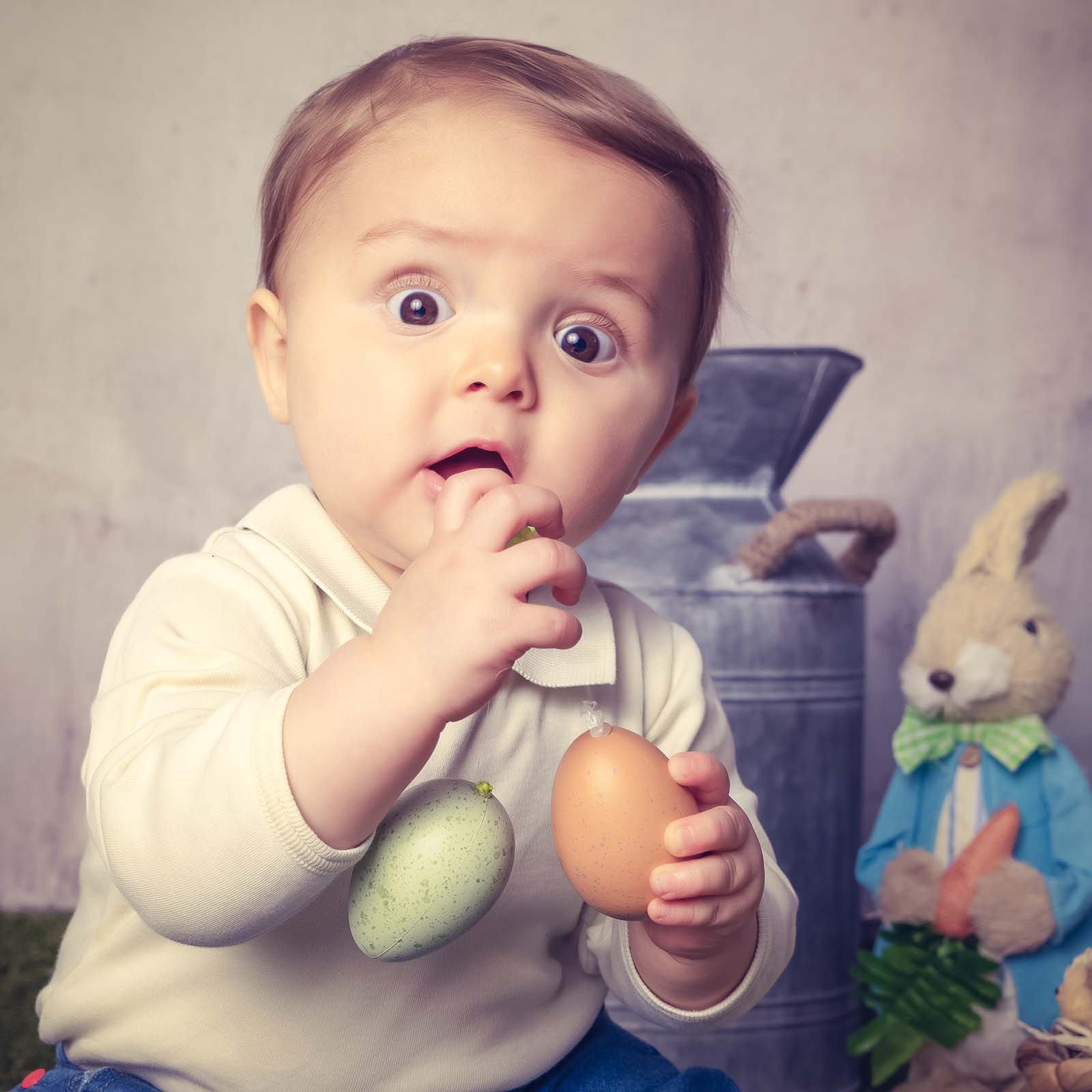 portrait d'un bébé avec de grands yeux surpris qui fait tomber deux œufs en plastique