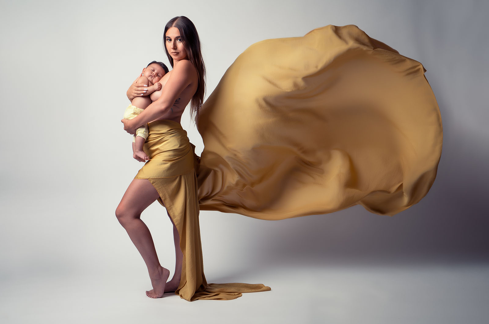 portrait d'une femme tenant son enfant dans les bras contre sa poitrine habillée d'un voile jaune volant