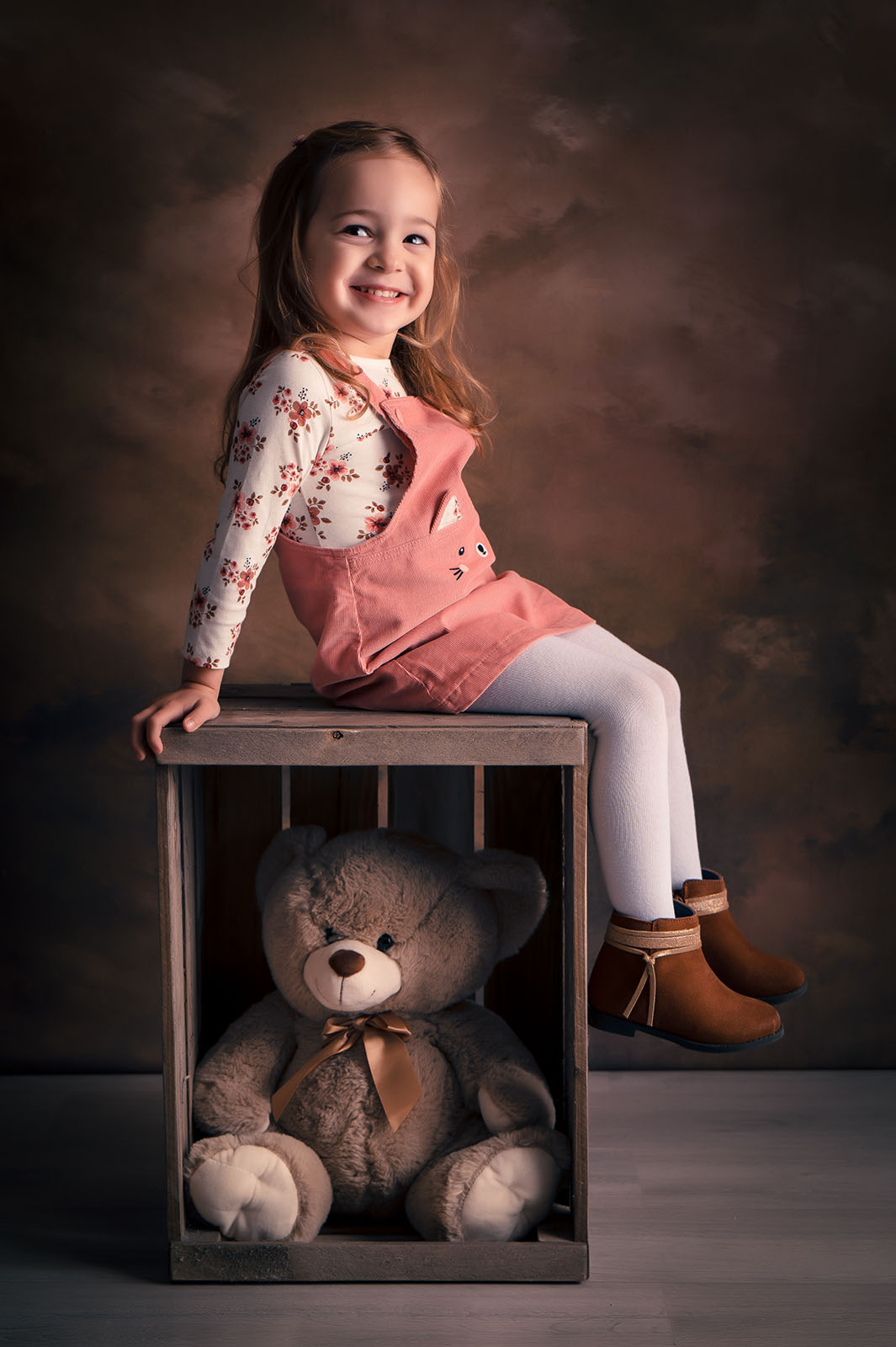 petite fille assise sur une caisse en bois avec un nounours dedans