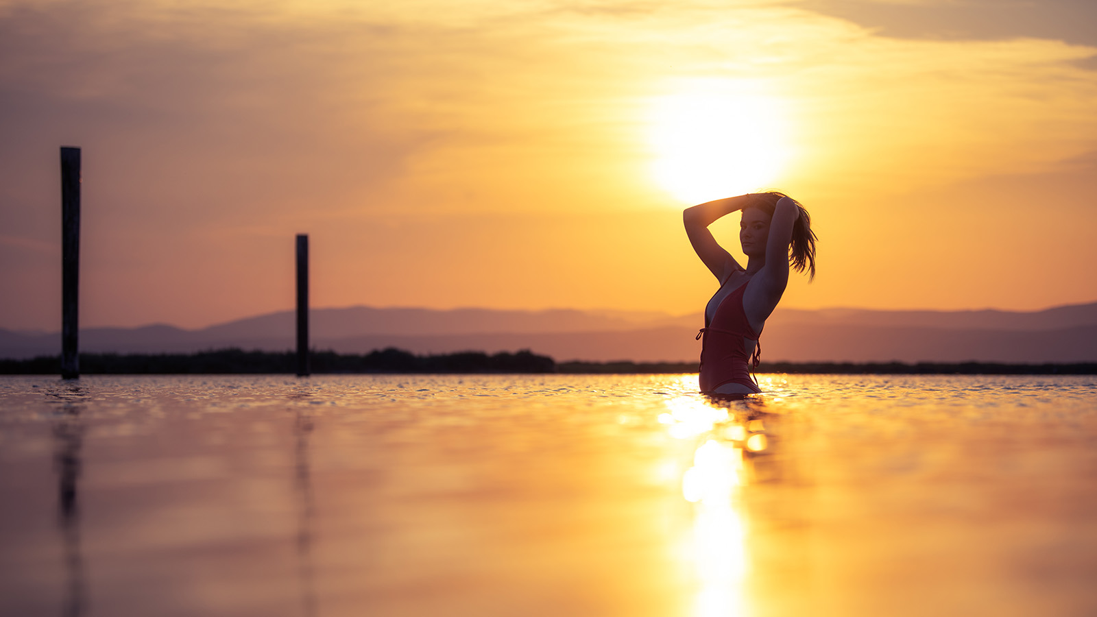 femme en maillot de bain rouge dans l'eau au coucher de soleil