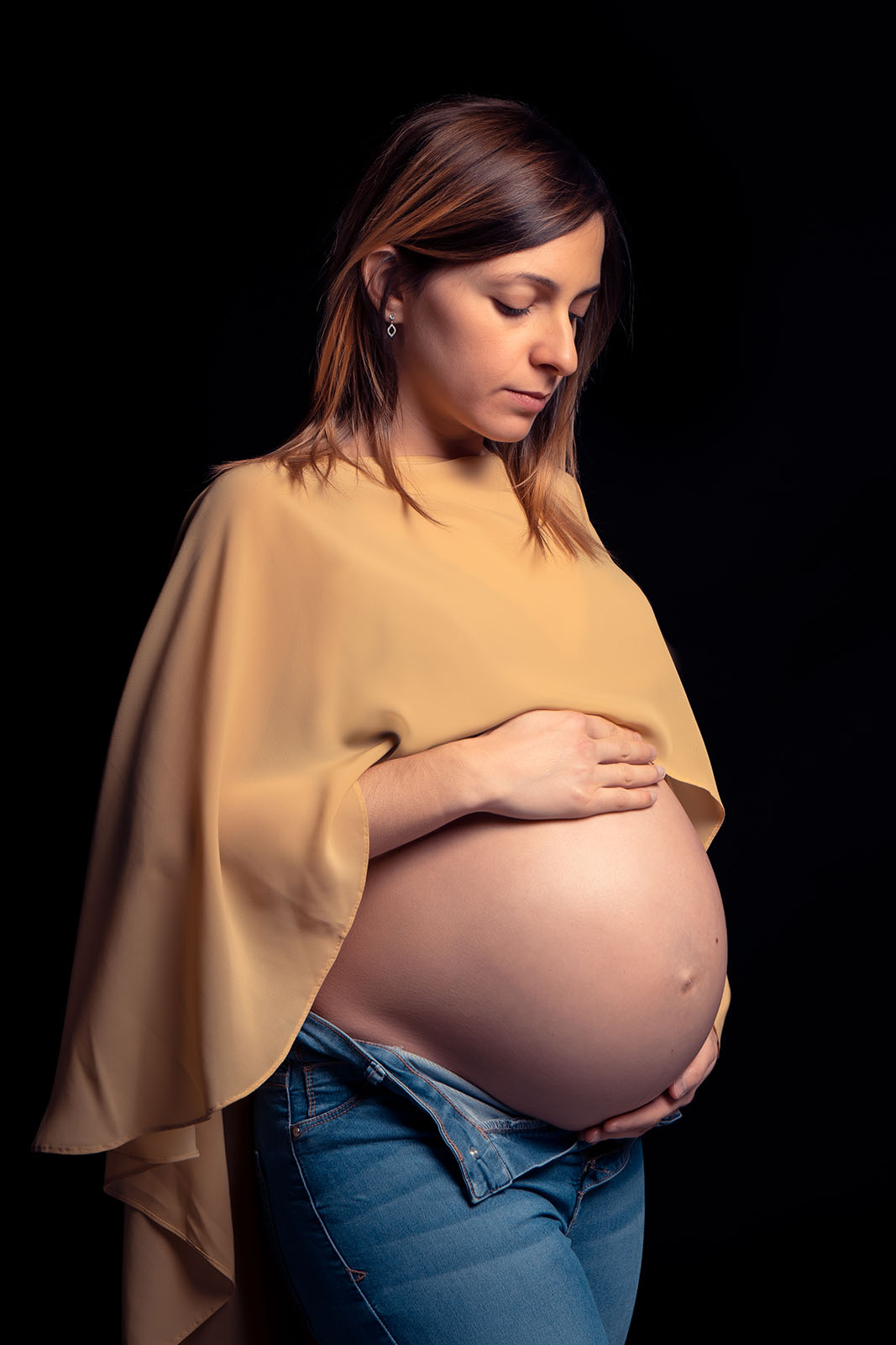 femme enceinte vêtue d'une cape jaune qui laisse son ventre à nu. En bas elle porte un jean bleu clair