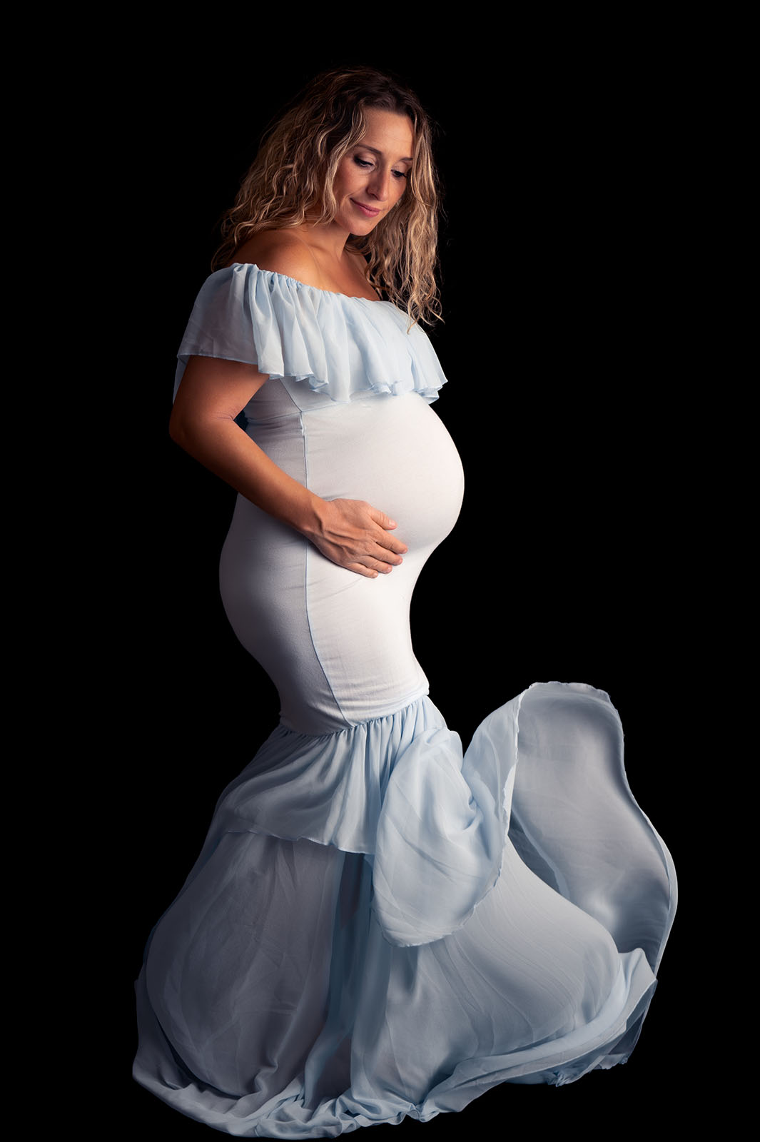 femme enceinte blonde vêtue d'une robe bleue claire moulante avec un petit voile au niveau du pied