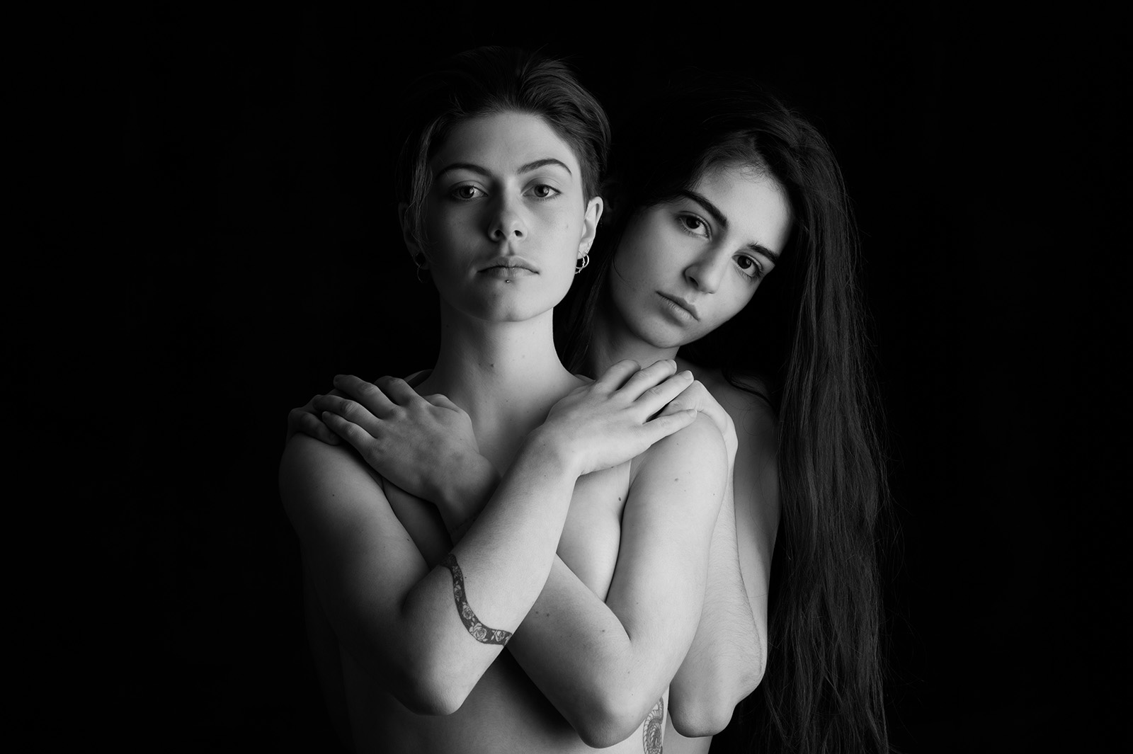 portrait studio noir et blanc de deux jeunes femmes l'une derrière l'autre, la première se cache la poitrine avec les bras