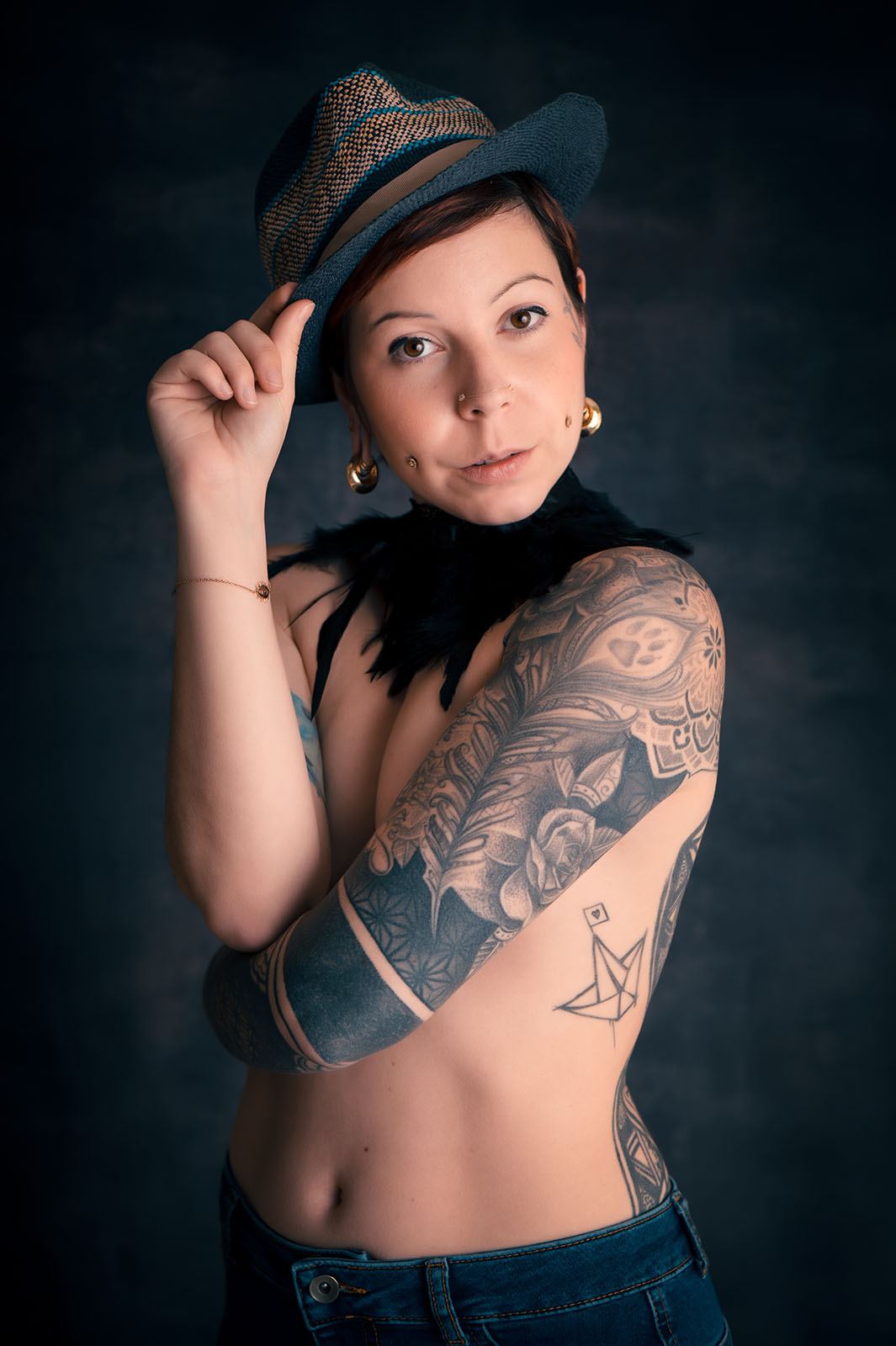 portrait studio d'un femme tatouée tenant un chapeau positionné sur sa tête