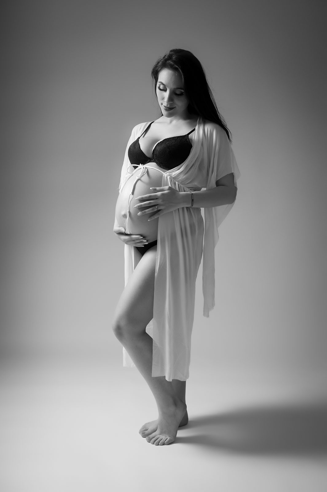femme enceinte en soutien gorge noir et peignoir fin en dentelle. Elle regarde son ventre