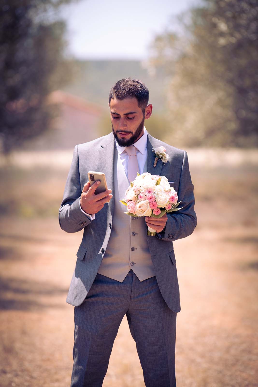 marié regardant son téléphone et portant le bouquet de fleur de la mariée