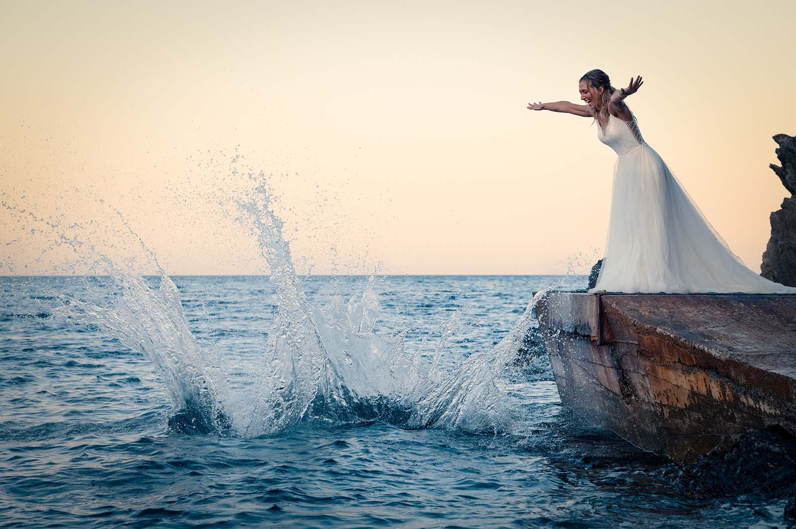 mariée au bord de l'eau sur un ponton se penchant en avant les bras écartés , on y voit un gros splash dans l'eau