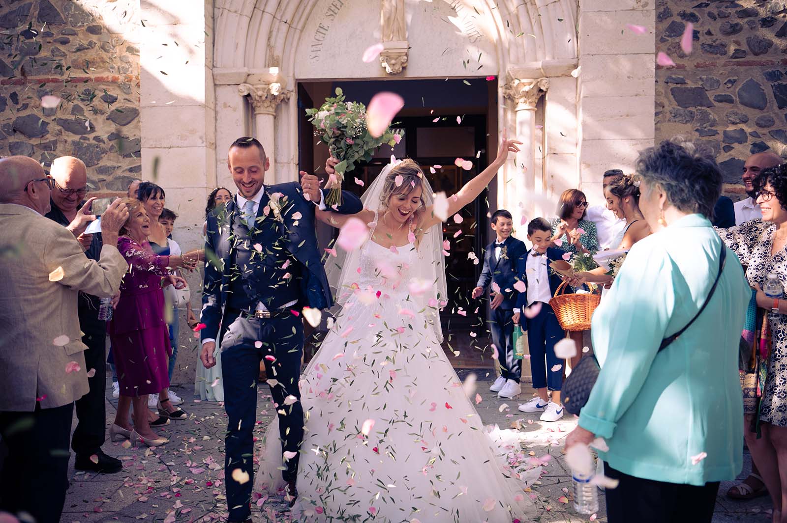 couple de mariés sortant d'une église avec des pétales de roses et des feuilles d'olivier