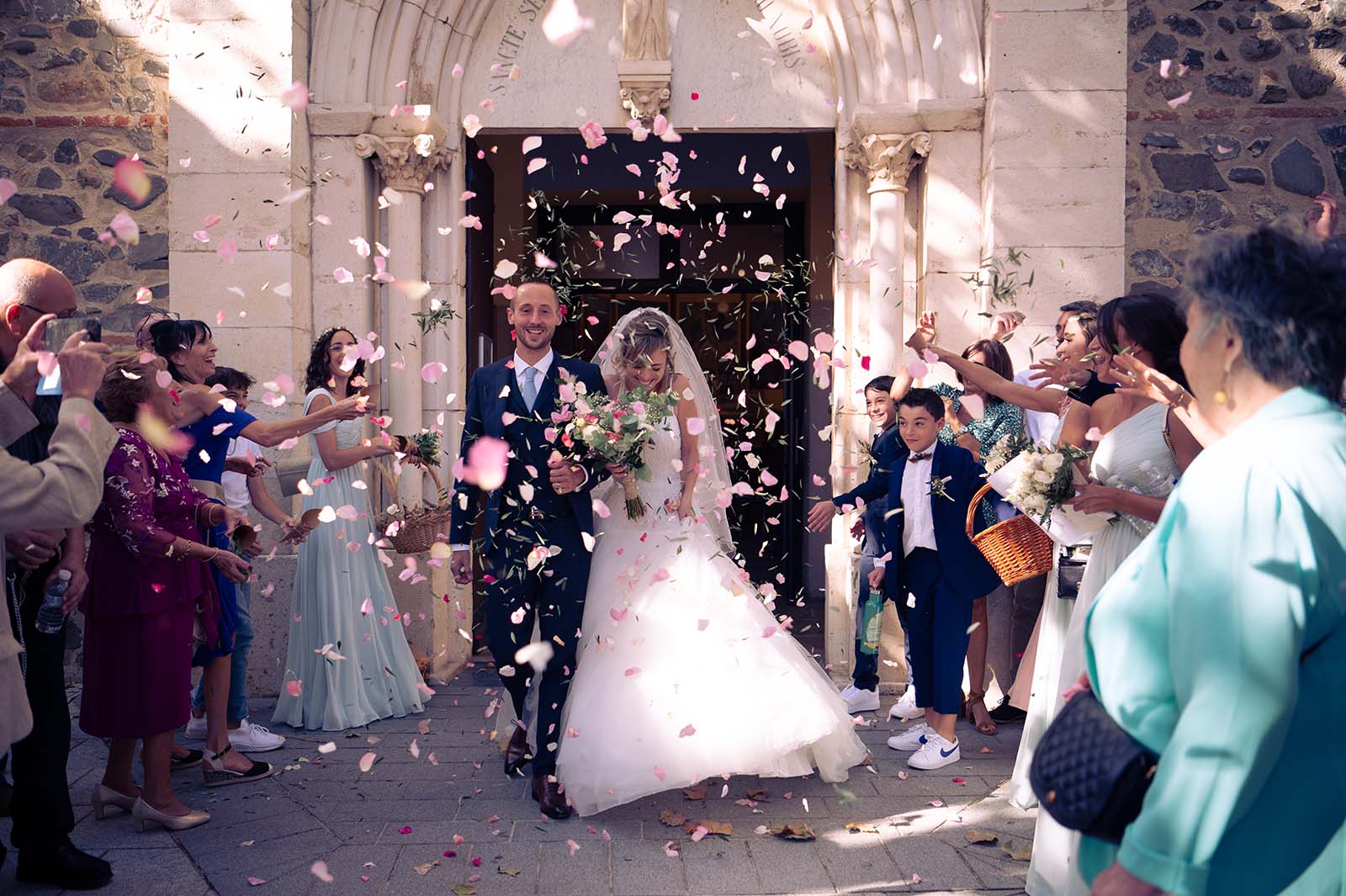 couple de mariés sortant d'une église avec des pétales de roses et des feuilles d'olivier