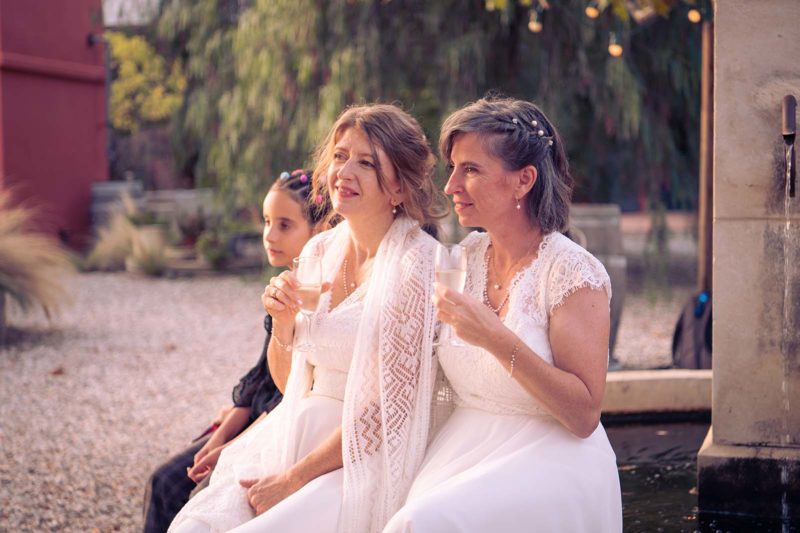 photos de deux femmes habillées en robe de mariée et tenant un verre de champagne à la main