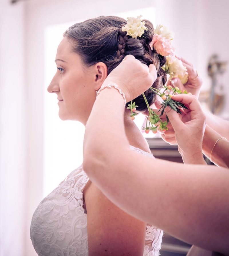 gros plan sur la coiffure d'une mariée où des mains sont en train de mettre des fleurs dans les cheveux